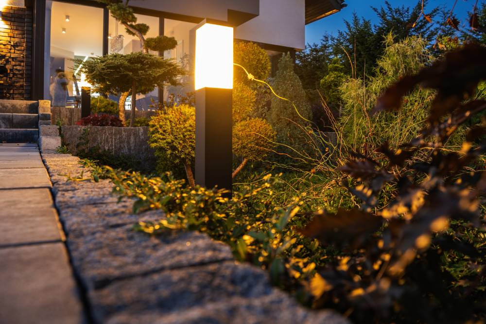 The focus is on the outdoor lighting next to a home path. The light is surrounded by greenery.