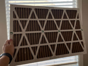 A furnace filter (specifically a disposable or pleated filter) being held up to the light to check whether it is time for it to be replaced.